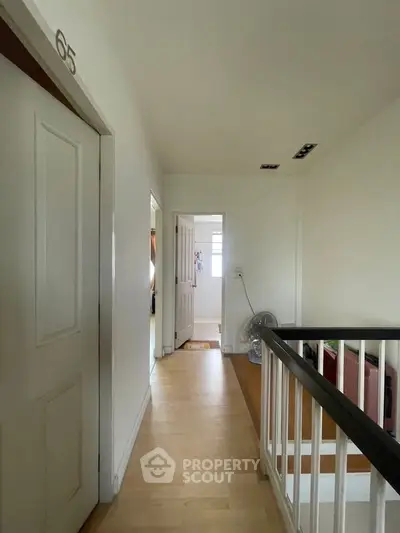 Bright hallway with wooden flooring and white walls, leading to multiple rooms.
