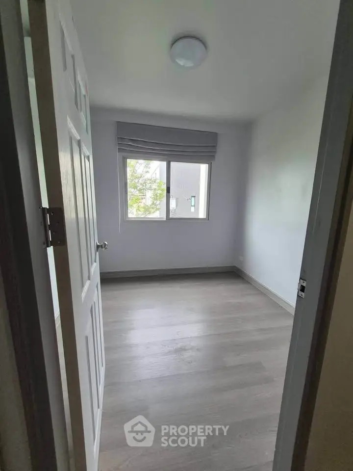 Bright empty bedroom with large window and wooden flooring, perfect for customization.