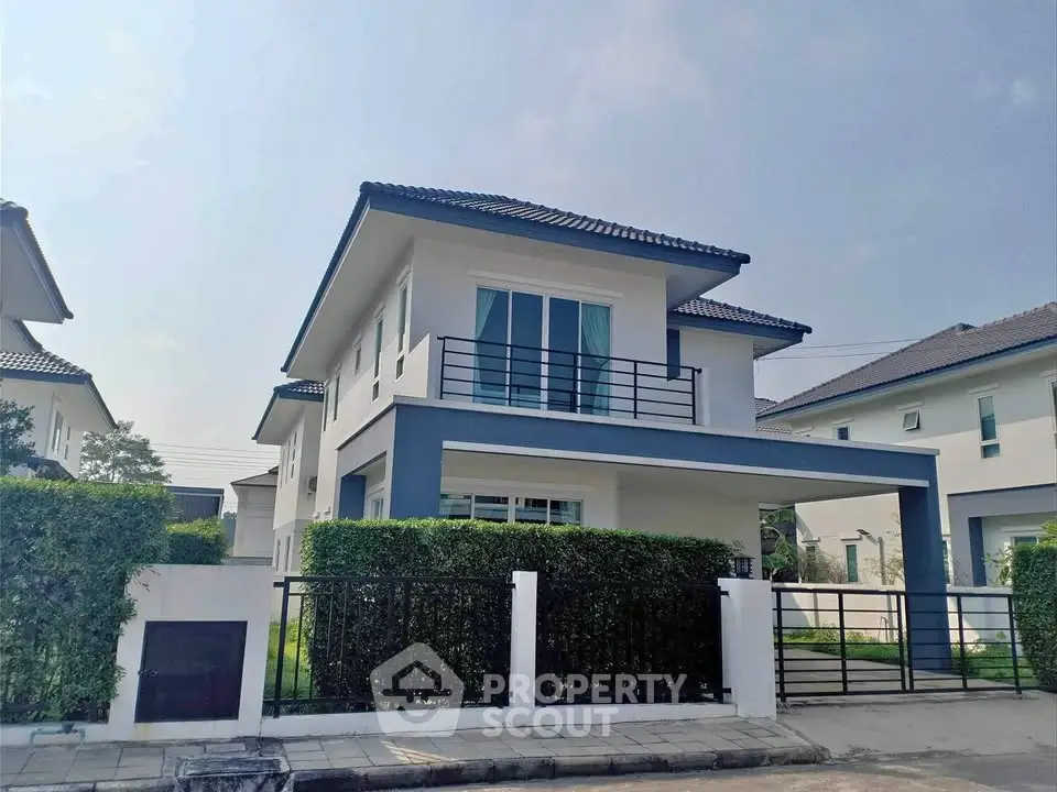 Modern two-story house with balcony and lush greenery in a serene neighborhood.