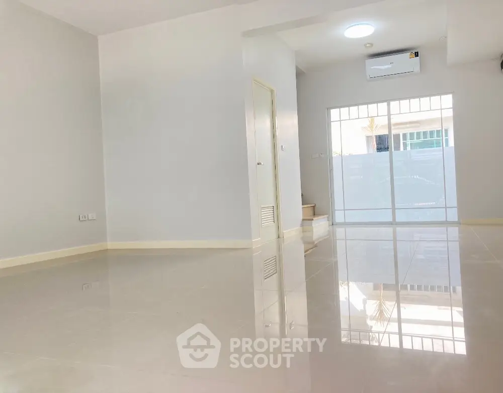 Spacious and bright living room with glossy tiled flooring, large windows allowing ample natural light, and a modern air conditioning unit, perfect for comfortable urban living.