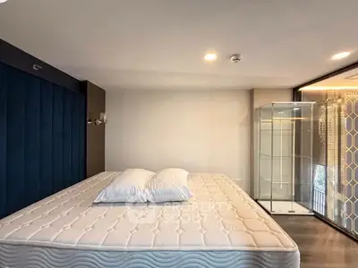 Modern bedroom with large mattress and glass shower enclosure, featuring elegant lighting and sleek design.