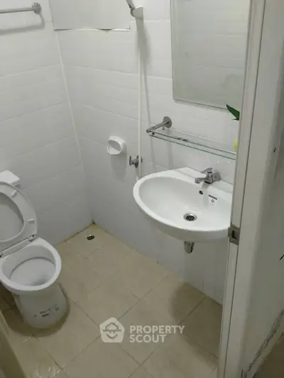 Compact bathroom with white tiles, toilet, sink, and shower area in a modern apartment.