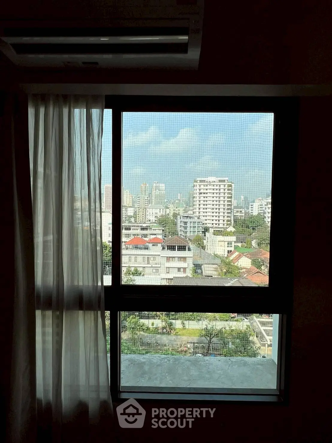 Stunning cityscape view from a modern apartment window with sheer curtains.