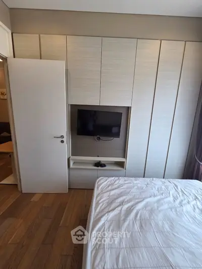 Modern bedroom with built-in wardrobe and wall-mounted TV, featuring sleek design and wooden flooring.