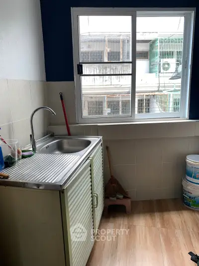 Cozy kitchen with window view, featuring a stainless steel sink and tiled backsplash, perfect for urban living.