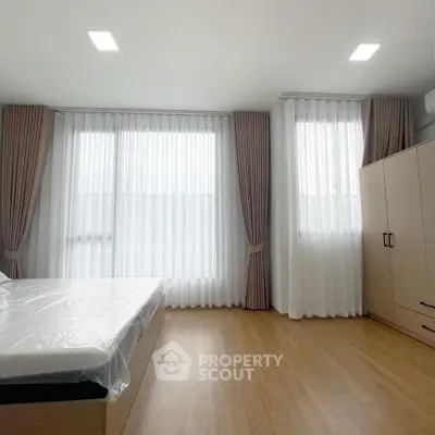 Spacious bedroom with large windows and elegant curtains, featuring a modern bed and ample storage.