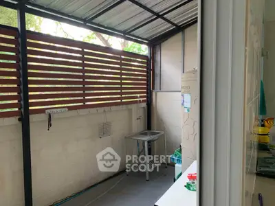 Charming covered balcony with utility area and lush greenery view, perfect for relaxation and practical use.