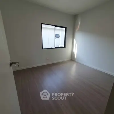 Spacious empty bedroom with large window and wooden flooring