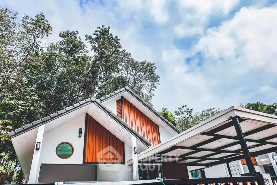 Modern architectural home with unique roof design and lush greenery surroundings.