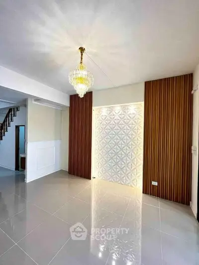 Elegant living room with chandelier and modern wall design, featuring glossy tiled flooring and wooden accents.