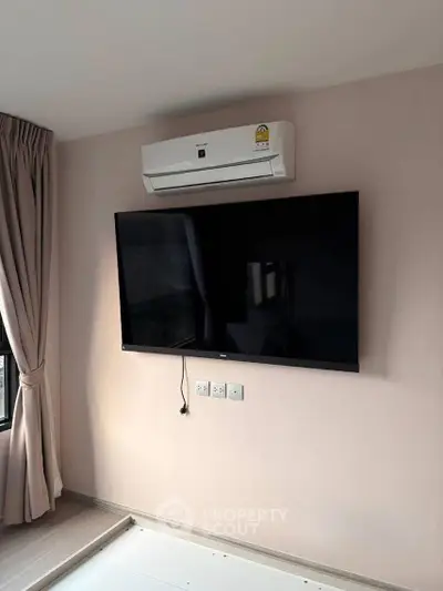 Modern living room with wall-mounted TV and air conditioning unit, featuring elegant curtains and neutral decor.