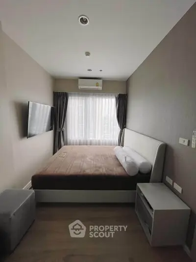 Cozy bedroom with modern decor, featuring a wall-mounted TV and large window for natural light.