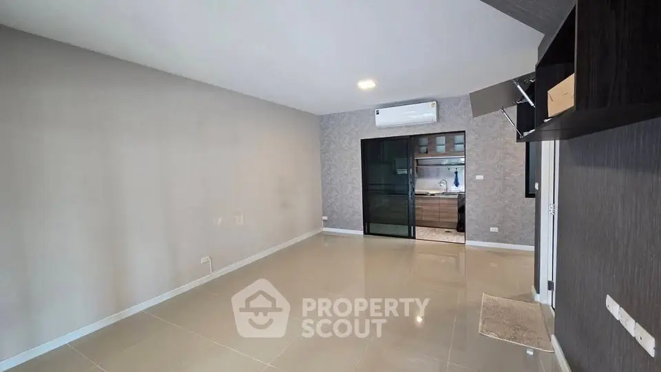 Spacious modern living room with sleek tile flooring and glass sliding doors leading to a stylish kitchen.