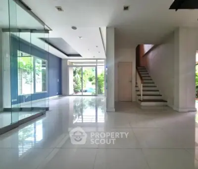 Spacious modern living area with glass walls and staircase, perfect for family gatherings.