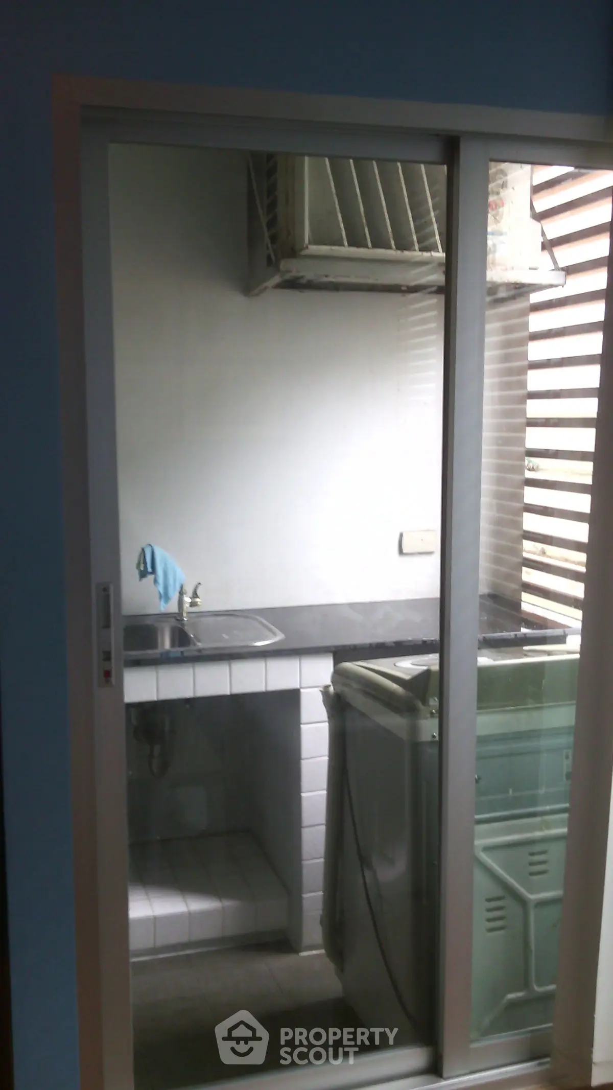 Compact kitchen area with washing machine and sink, featuring a sliding glass door.