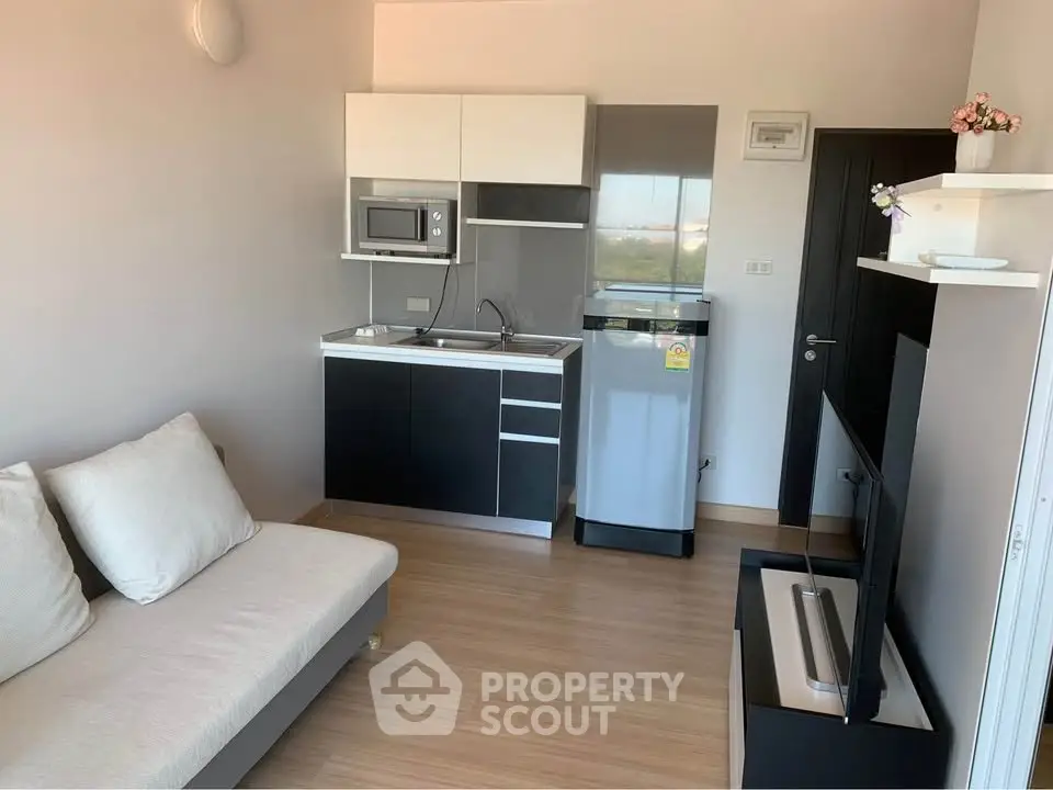 Modern compact living room with kitchenette, featuring sleek black and white cabinetry and cozy seating.