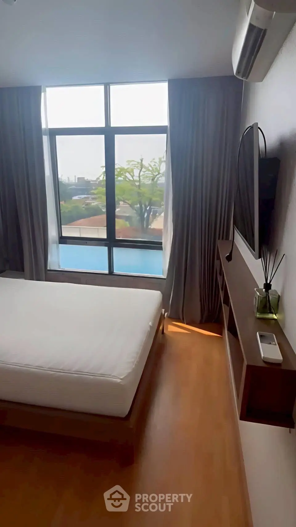 Modern bedroom with large window and pool view, featuring sleek wooden flooring and minimalist decor.