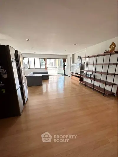 Spacious open-plan living room with large windows and wooden flooring in modern apartment.