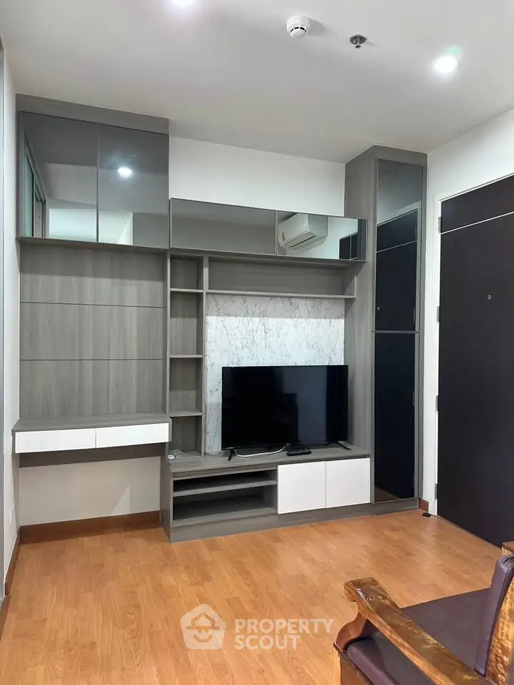 Modern living room with sleek built-in shelving and TV, featuring wood flooring and contemporary design.