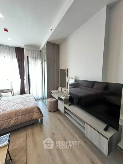 Modern bedroom with sleek design, large TV, and natural light from floor-to-ceiling windows.