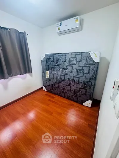 Cozy bedroom with wooden flooring and air conditioning, featuring a neatly wrapped mattress against the wall.