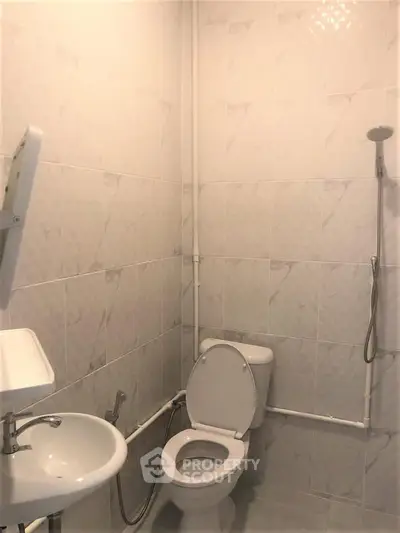 Compact bathroom with white tiles, toilet, sink, and shower head, ideal for efficient space use.