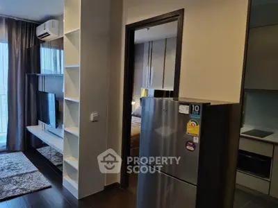 Modern studio apartment with sleek furniture and stainless steel fridge, showcasing a comfortable living space that seamlessly blends into a cozy bedroom area.