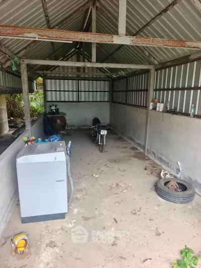 Spacious garage with metal roof and washing machine, ideal for storage or workshop use.