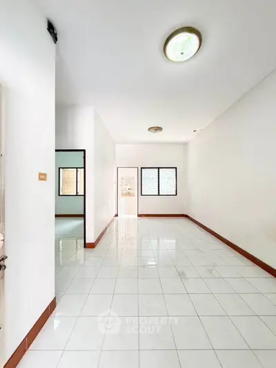 Spacious empty room with white tiled floor and bright natural light, ideal for customization.