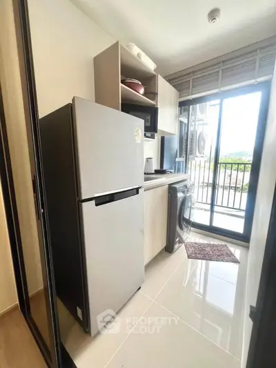 Modern kitchen with stainless steel fridge and washing machine, bright natural light from large window.