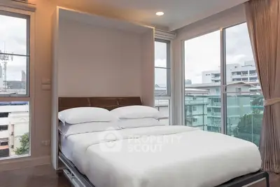 Modern bedroom with large windows and city view, featuring a comfortable bed and elegant decor.