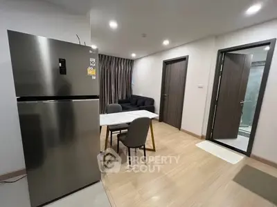 Modern apartment interior with sleek kitchen and cozy living area, featuring a stainless steel fridge and elegant dining setup.
