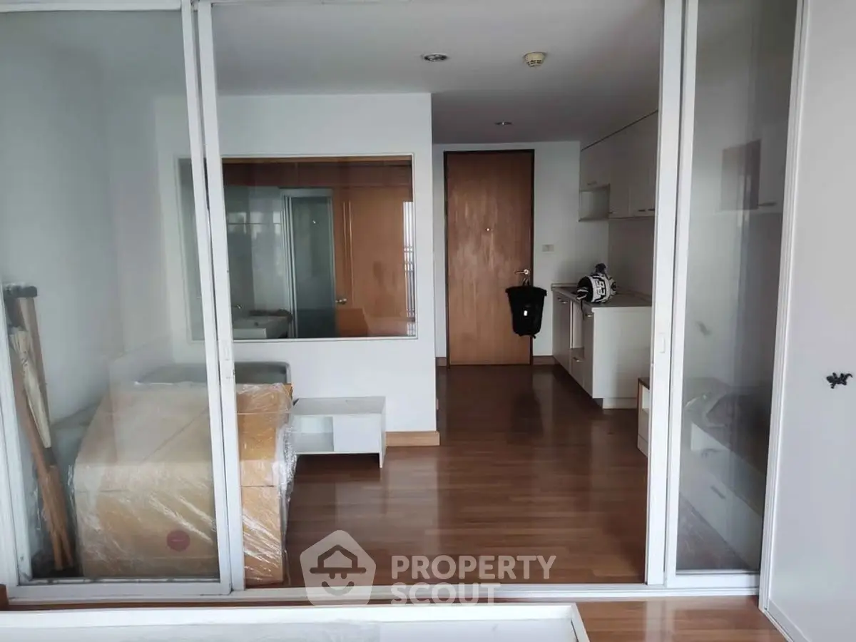 Modern studio apartment with wooden flooring and glass partition, featuring a compact kitchen and cozy living space.