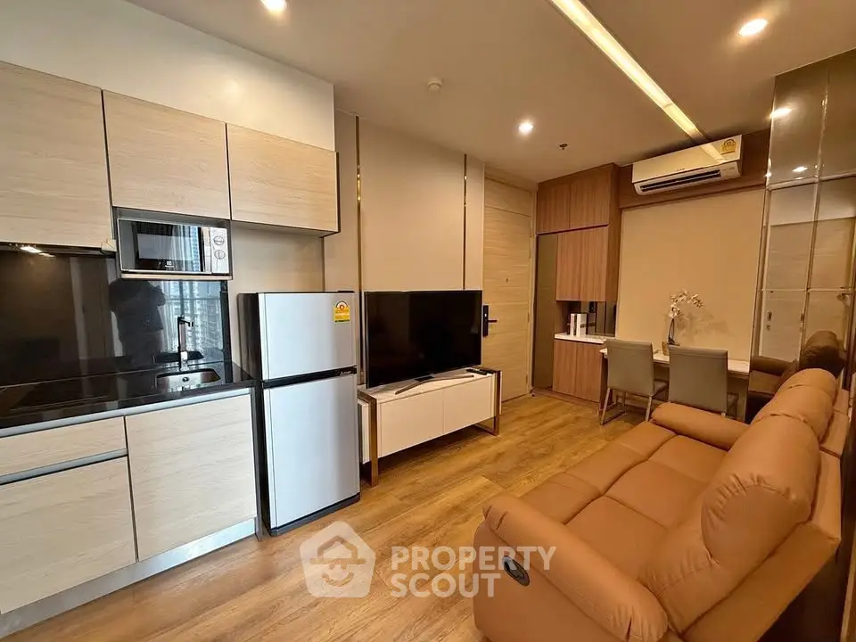 Modern living room with open kitchen, featuring sleek appliances and cozy seating area.