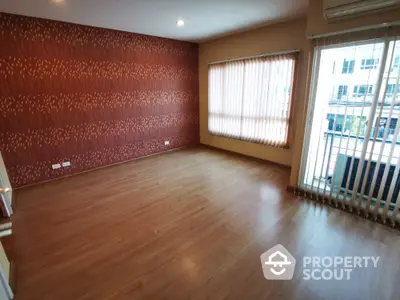 Spacious living room with elegant hardwood flooring and a unique textured accent wall, ample natural light from large window, and a cozy balcony.