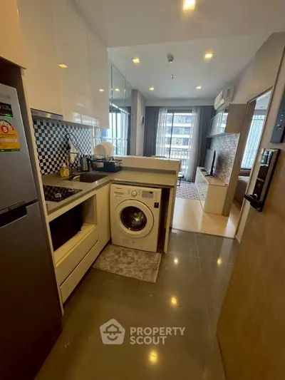 Modern kitchen with washing machine and open layout leading to living area.