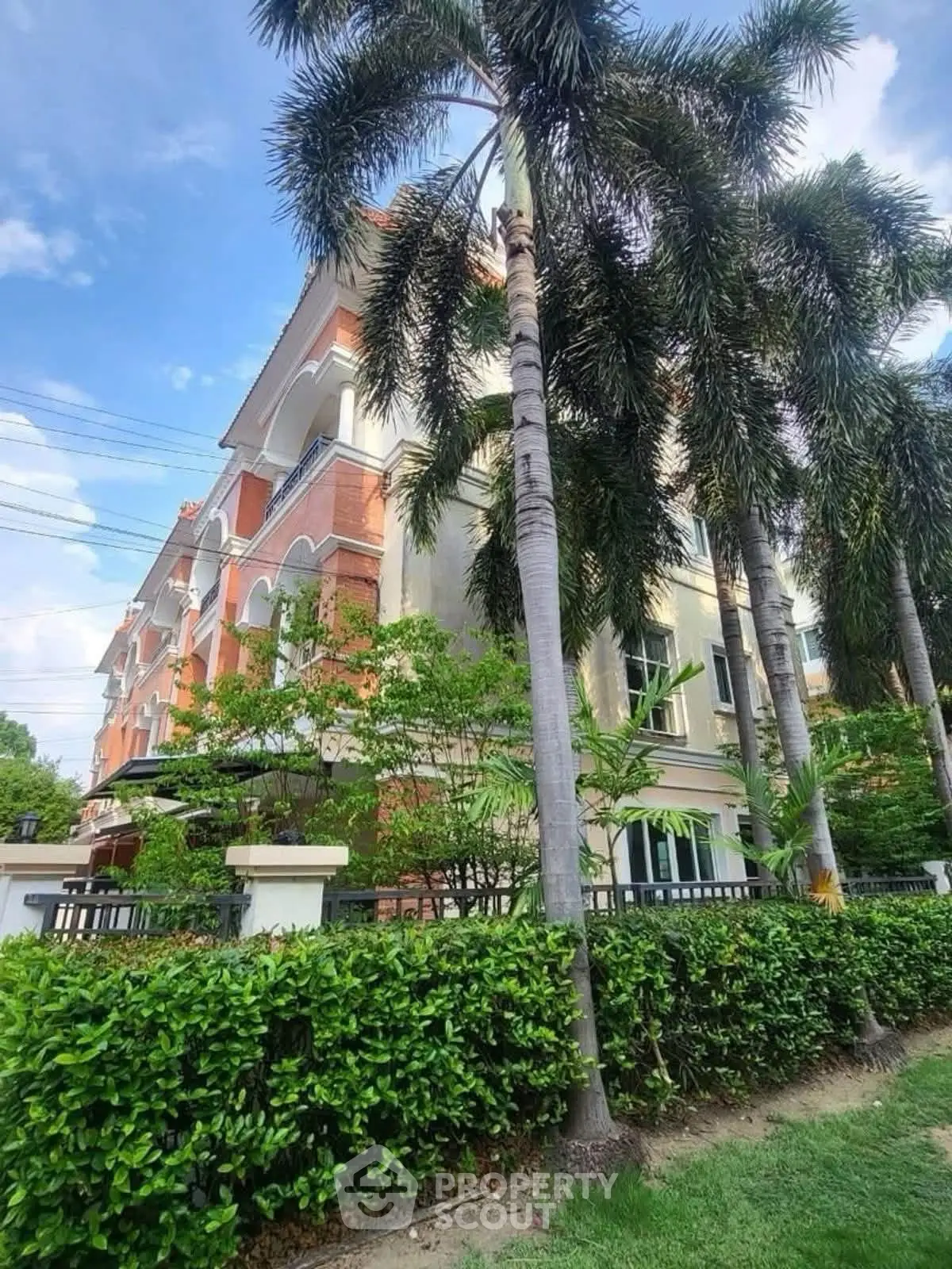 Elegant multi-story building with lush greenery and palm trees, showcasing classic architecture and vibrant surroundings.