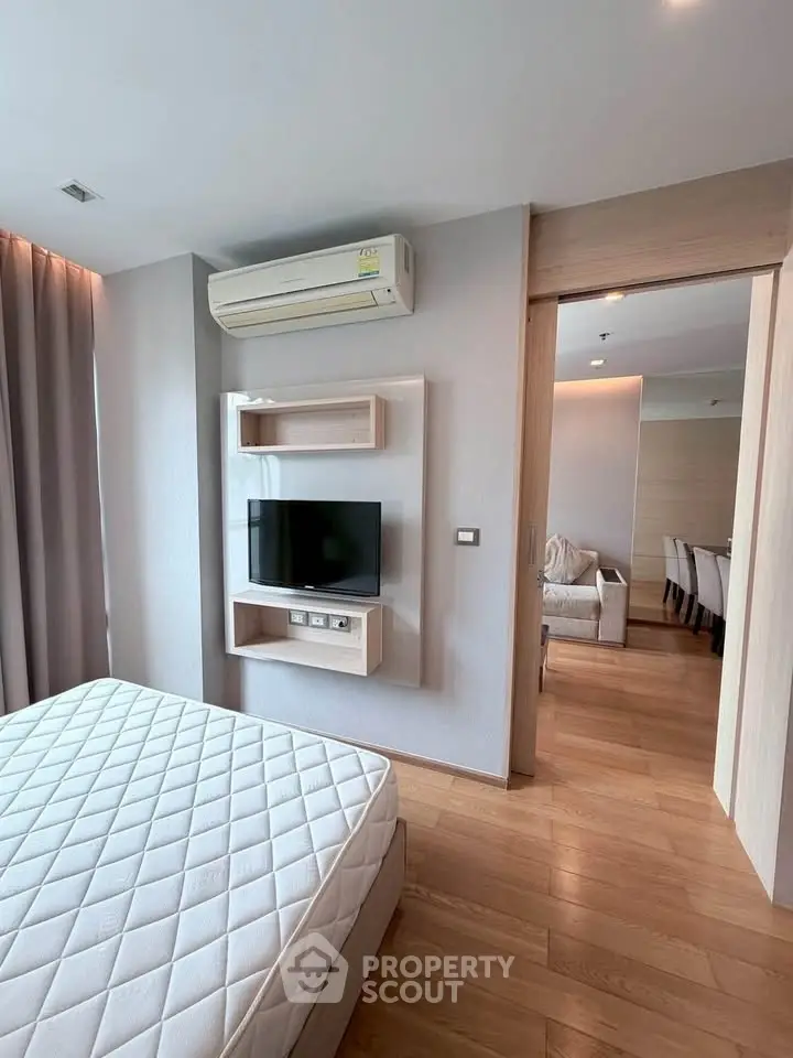 Modern bedroom with wall-mounted TV and air conditioning, featuring wooden flooring and sliding door to dining area.