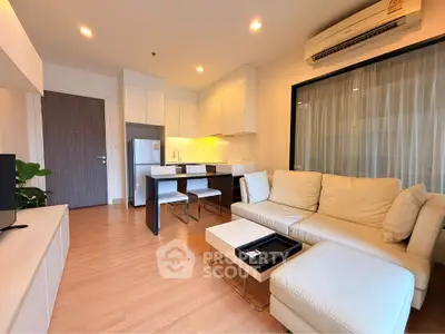 Modern living room with open kitchen, featuring sleek furniture and warm lighting.