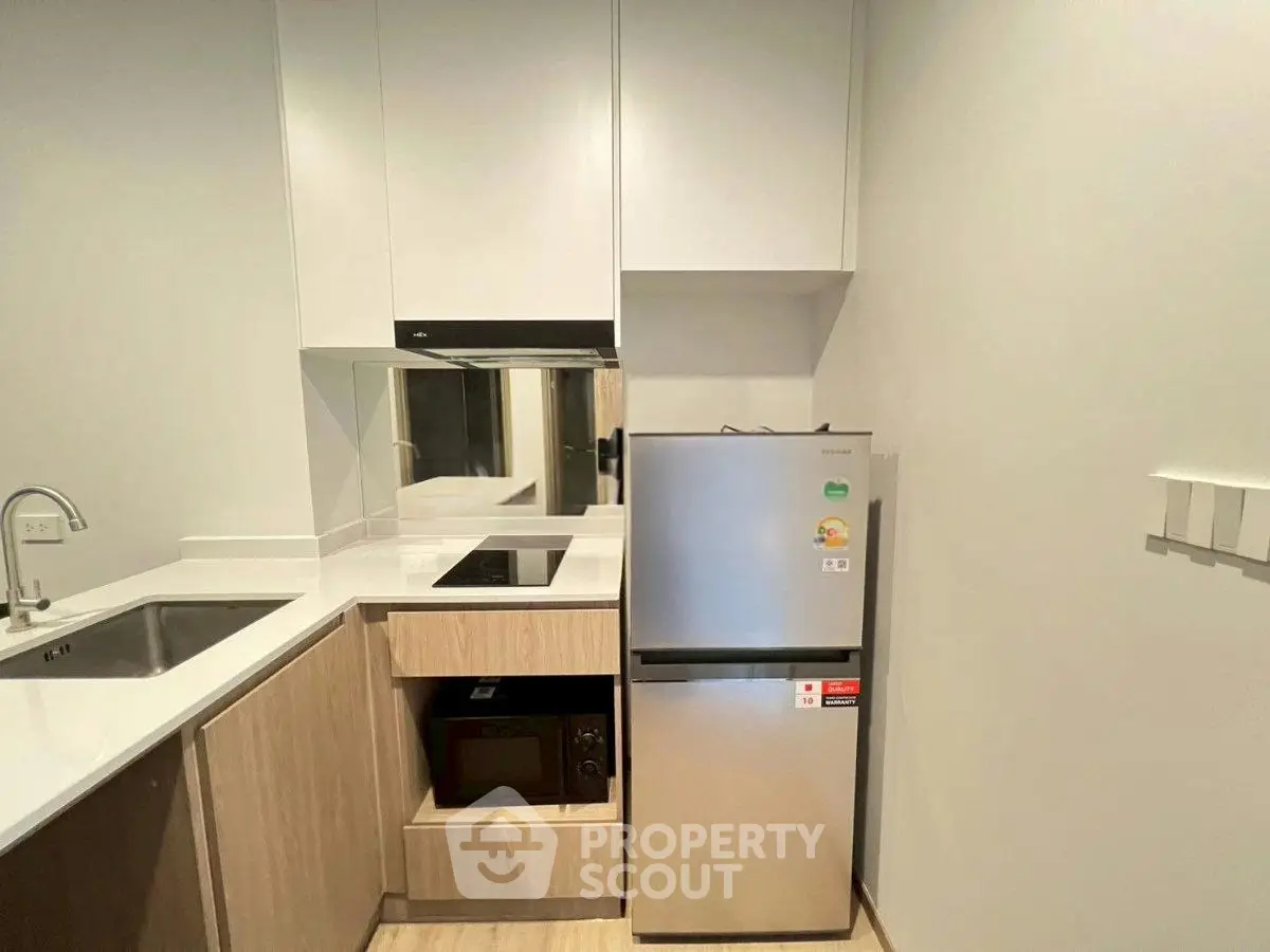 Modern kitchen with sleek appliances and minimalist design, featuring a compact fridge and built-in microwave.