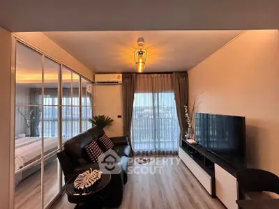 Modern living room with stylish decor and large TV, adjacent to a cozy bedroom with glass partition.