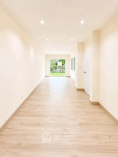 Spacious and bright empty room with wooden flooring and garden view.