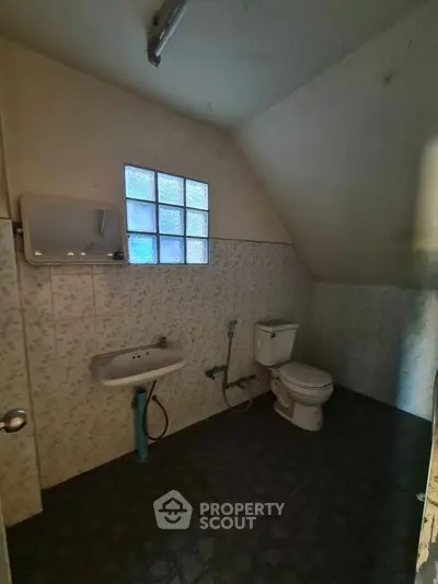 Cozy bathroom with sloped ceiling and frosted glass window, featuring a sink and toilet.