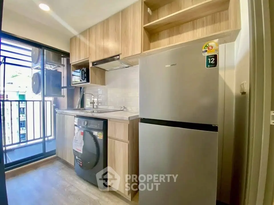 Modern kitchen with wooden cabinets, washing machine, and fridge in a bright apartment.