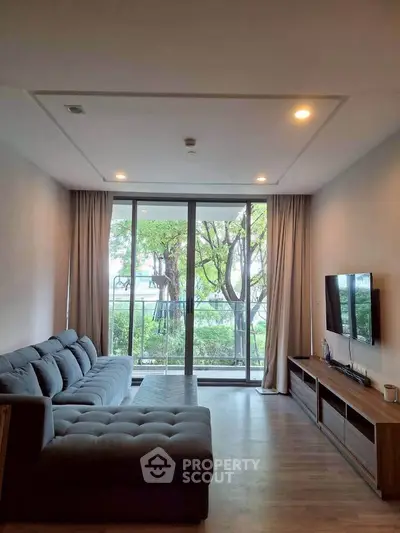 Spacious living room with large windows and modern decor, offering a serene view of lush greenery.