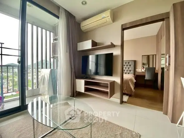 Modern living room with glass table and TV, adjacent to a cozy bedroom with scenic view.
