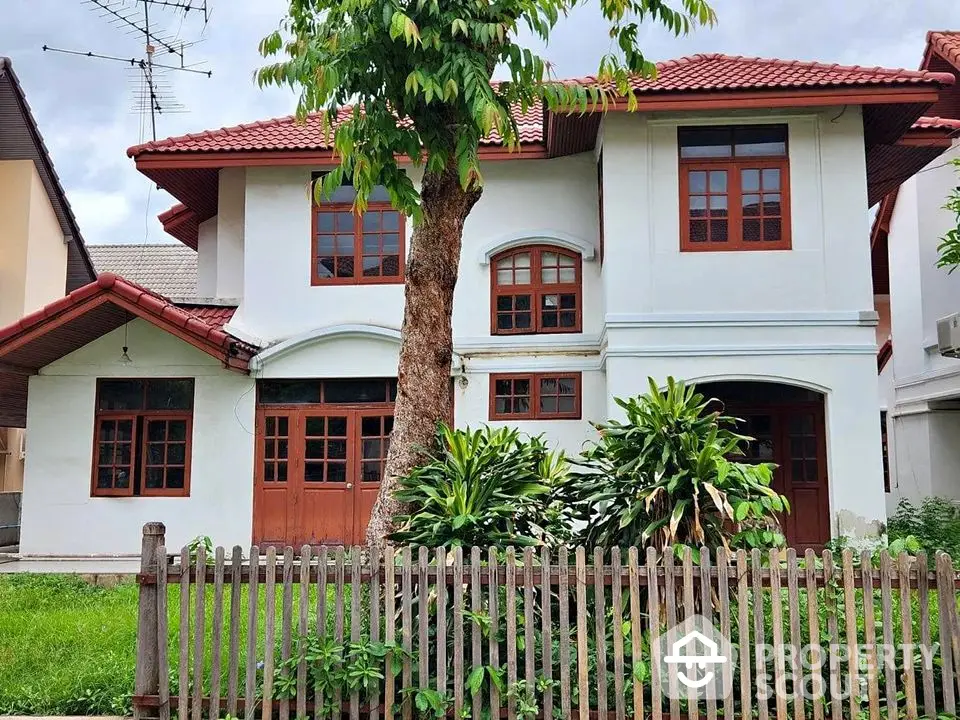 Charming two-story house with red roof and lush garden, perfect for family living.