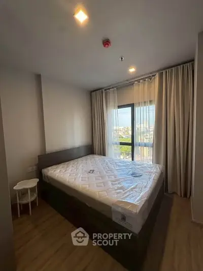 Cozy bedroom with large window offering city views, featuring a comfortable bed and modern decor.