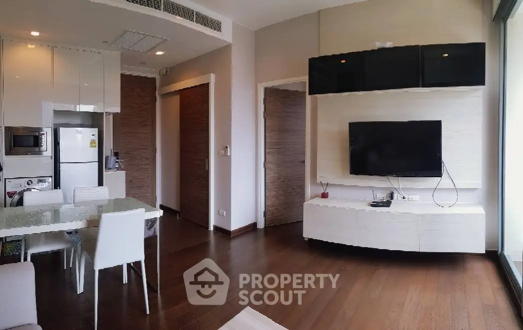 Modern living room with sleek furniture and open kitchen layout, featuring a wall-mounted TV and wooden flooring.