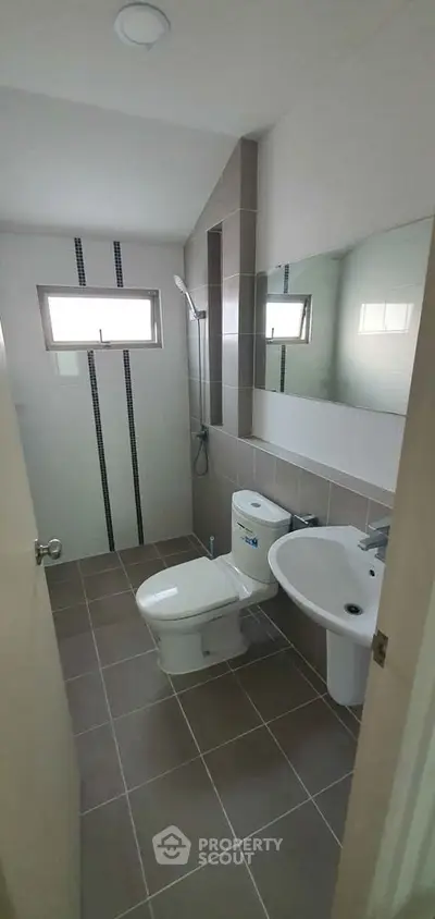 Modern bathroom with sleek design, featuring a toilet, sink, and shower area in a compact layout.